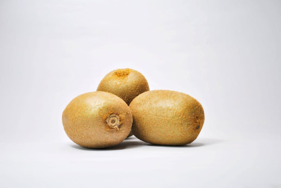 Three fresh kiwi fruits on a clean white surface, showcasing their natural texture.