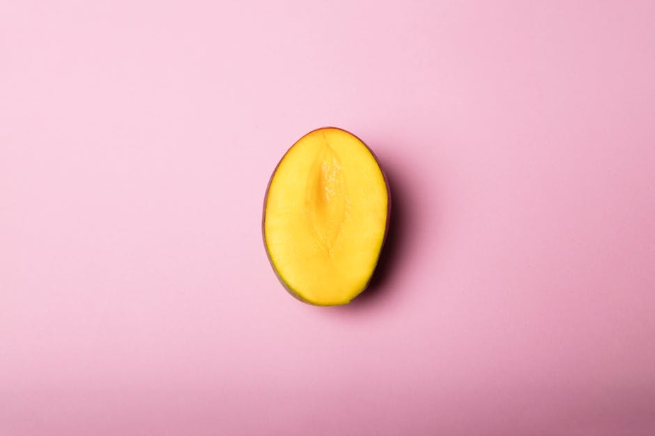 Half sliced mango placed on a soft pink background in a minimal flat lay style.