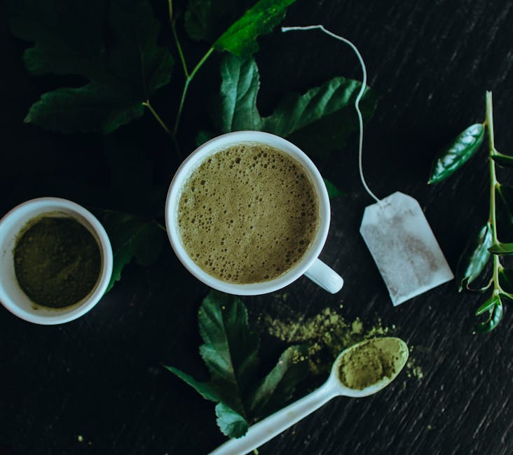 Top view of a refreshing matcha latte surrounded by leaves, powder, and a tea bag.