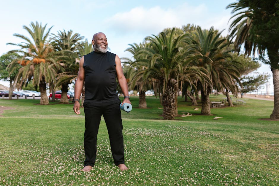 Elderly African American man doing yoga with a mat in a sunny park.