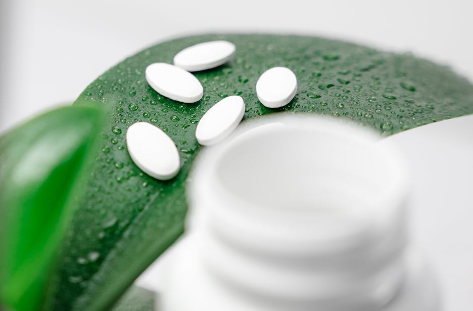 Close-up of white pills on a dew-covered leaf with a blurred bottle foreground.