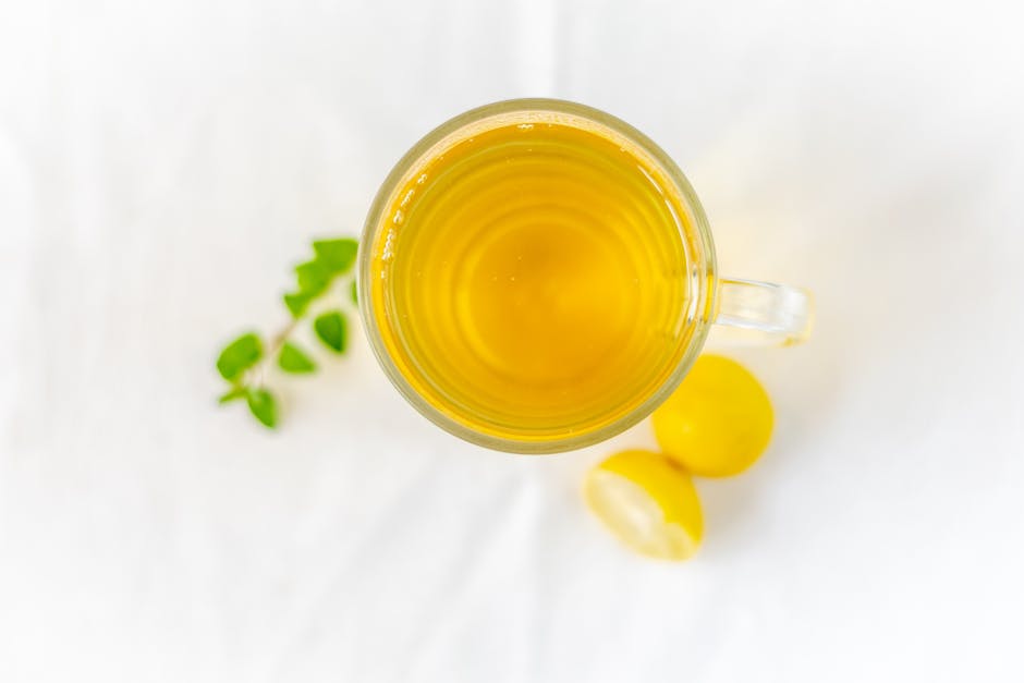 Refreshing lemon tea in a clear glass mug with fresh mint on a white surface.