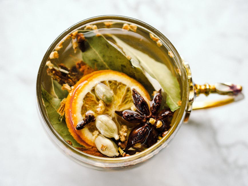 A top-view of herbal tea with citrus slices, star anise, and cardamom in an ornate cup.