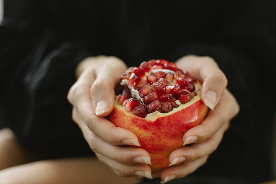 Crop anonymous female sitting with red pomegranate with juicy seeds for healthy organic diet