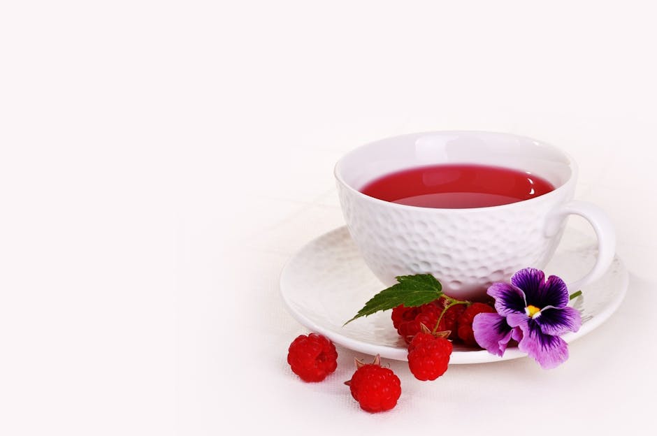 A vibrant raspberry tea in a ceramic cup with fresh raspberries and a pansy flower.