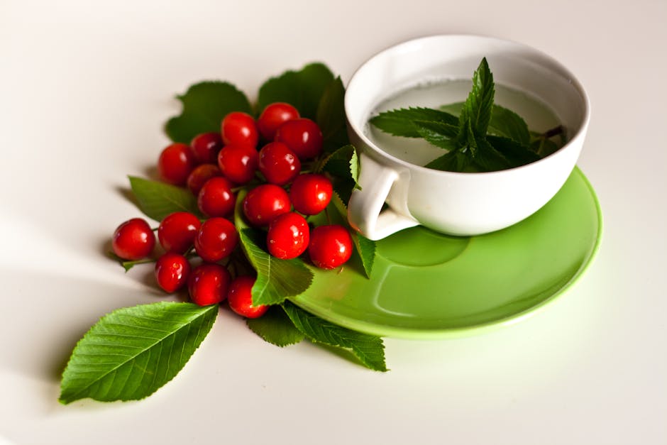 Refreshing mint tea in a white cup with cherries and green leaves on a green saucer.