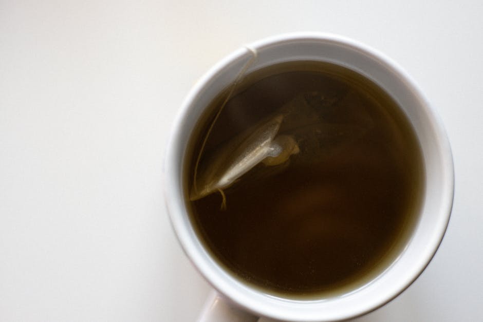 Top view of a white cup filled with fresh brewed green tea on a white background.