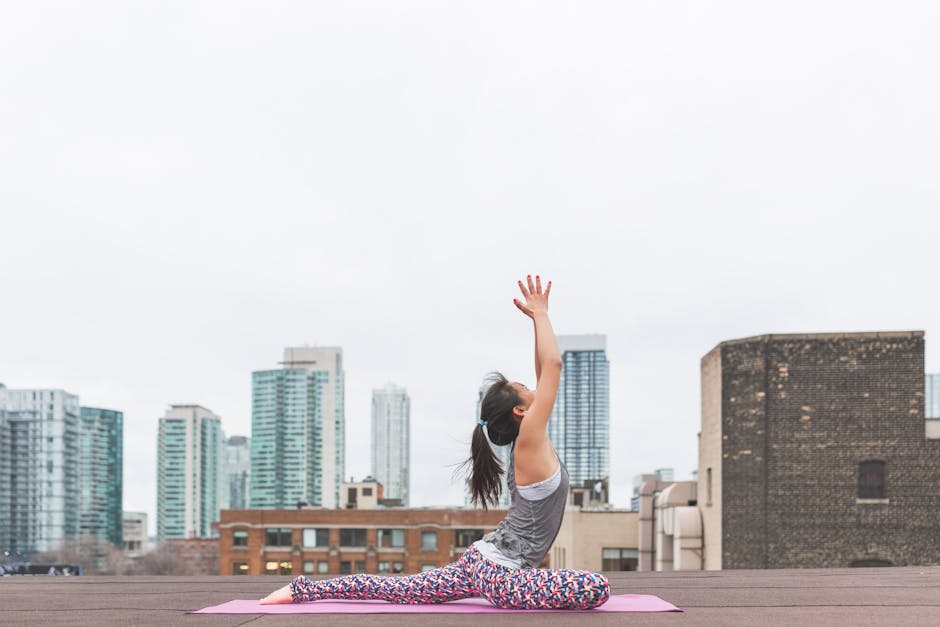 Adult woman doing yoga outdoors on a rooftop with city skyline in the background.