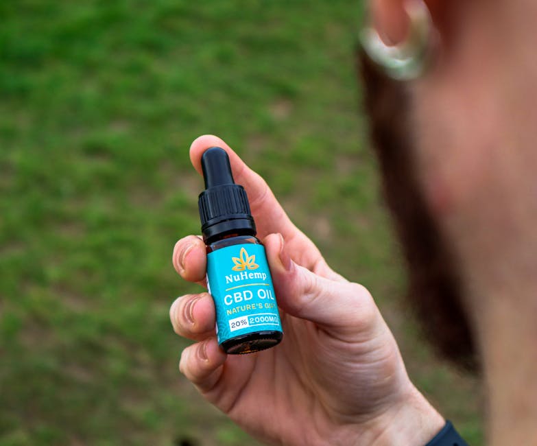 A person holding a NuHemp CBD oil bottle in a grassy outdoor setting, highlighting wellness.
