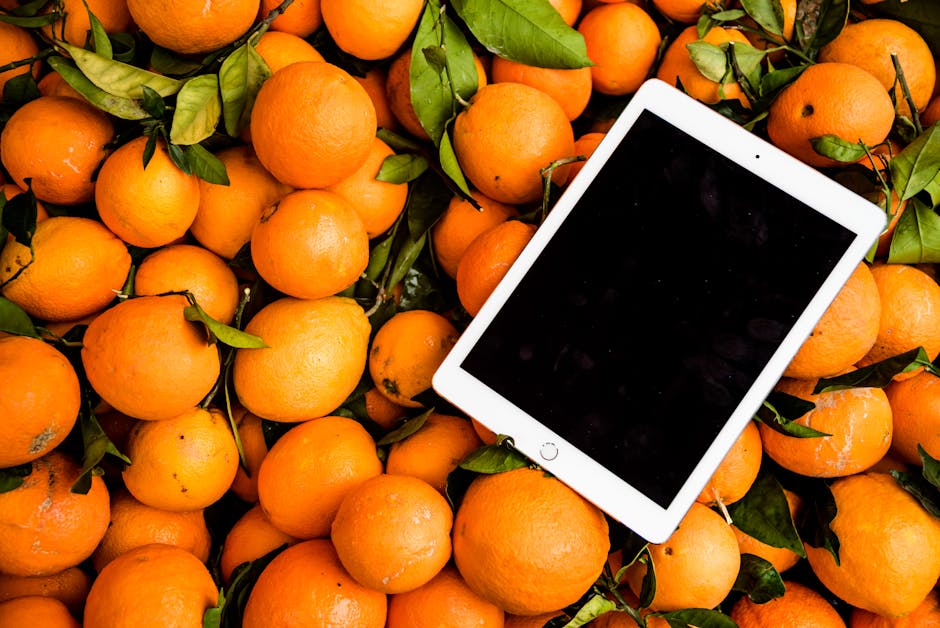 A vibrant collection of fresh oranges with a tablet, showcasing a mix of technology and nature.
