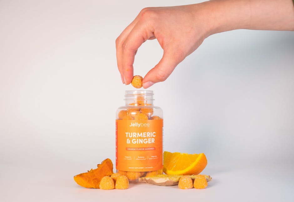 Close-up of a hand taking a turmeric and ginger gummy from a bottle, surrounded by ingredients.